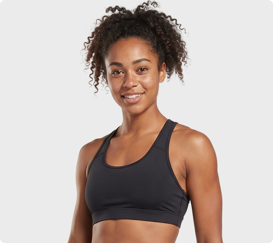 smiling woman wearing a black sports bra, posing in a studio with a light gray background.