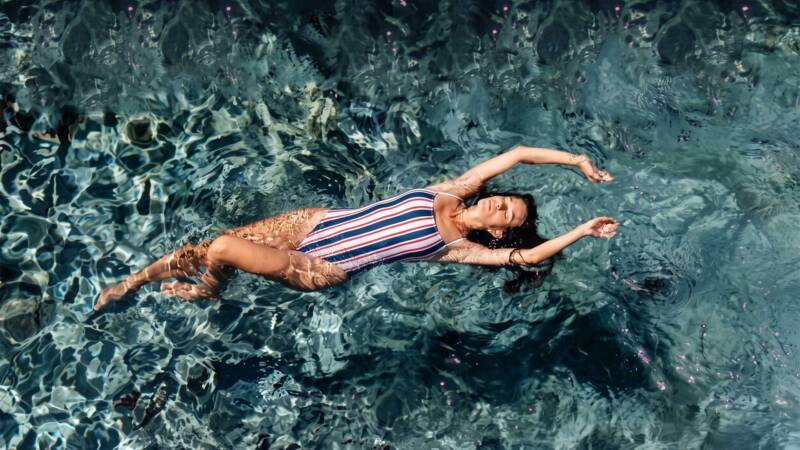 woman floating on her back in a striped swimsuit in clear blue water, relaxing with arms spread.