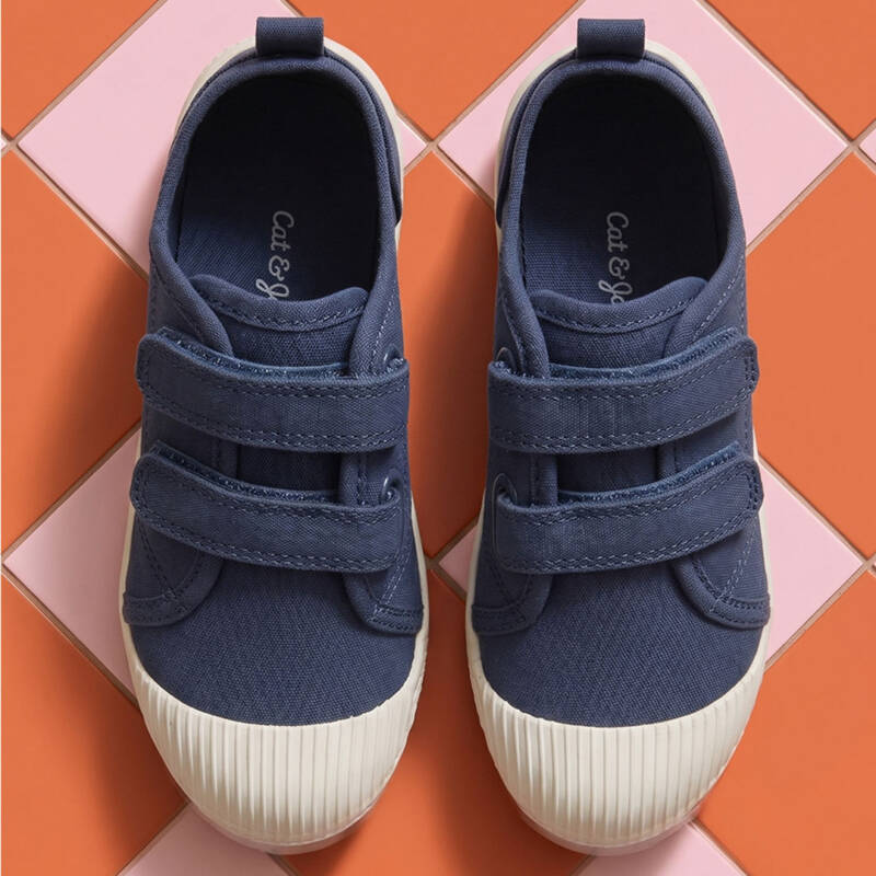 top-down view of two navy blue sneakers with two velcro straps and white rubber soles on an orange-pink tiled floor.