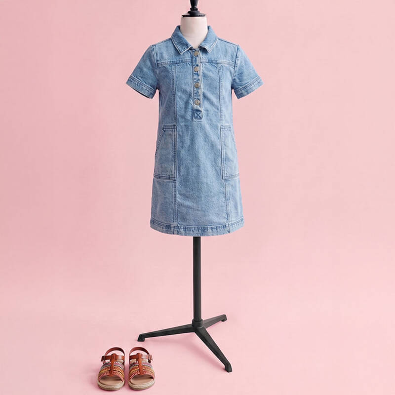 lightwash denim shirt dress on a mannequin with a pink backdrop, and brown strappy sandals on the floor in front.