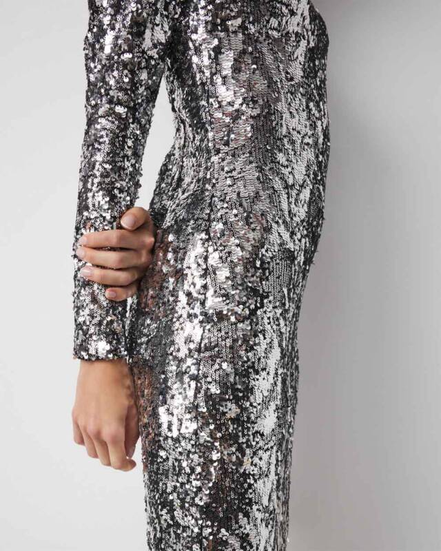 side view of a person wearing a silver sequined dress, with the arm bent and hand resting near the waist, the fabric densely covered in sequins.
