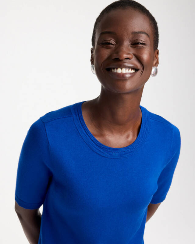 smiling black woman wearing a bright blue top, facing the camera in a portrait shot.