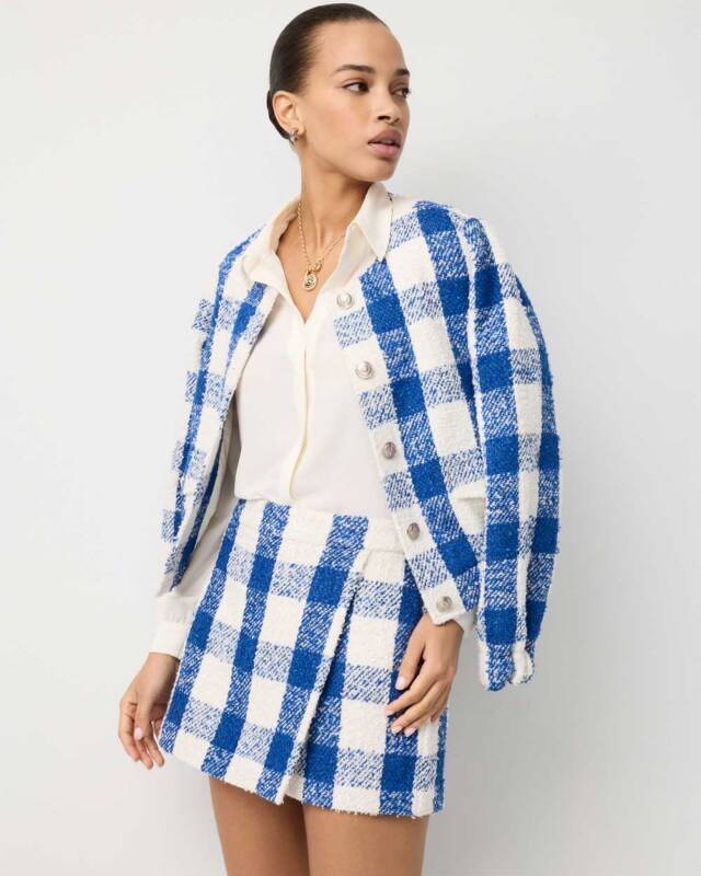 model wearing a blue-and-white checkered blazer draped over shoulders with a matching mini skirt and a white blouse.