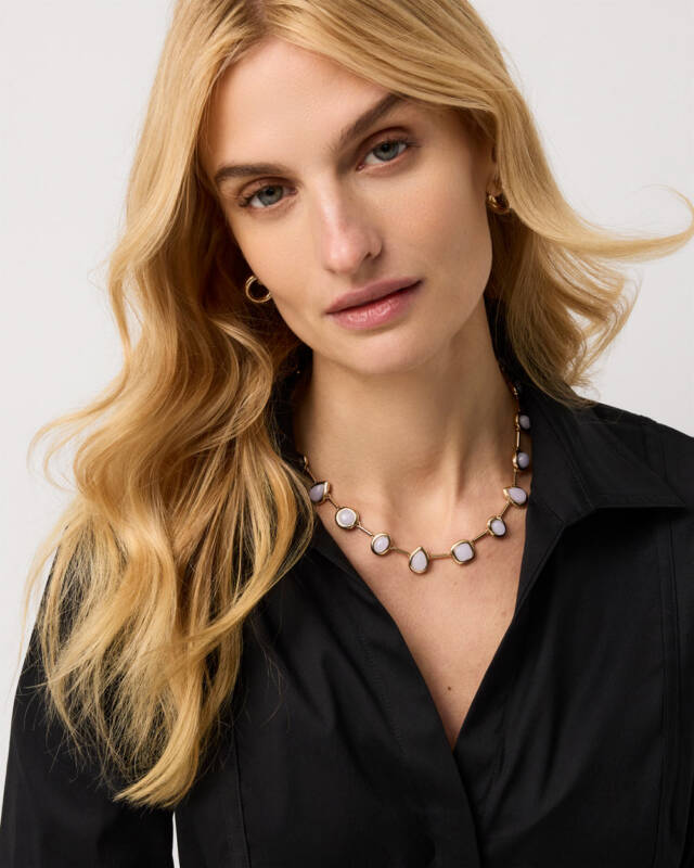close-up of a woman wearing a gold link necklace with pale purple stones, black blouse, soft blonde waves framing her face.