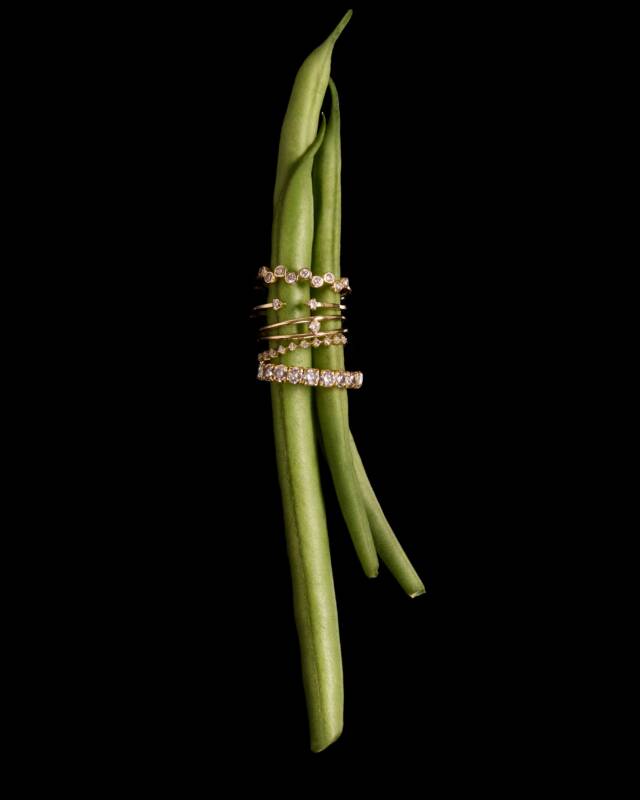 gold diamond-studded rings stacked around green beans against a black background