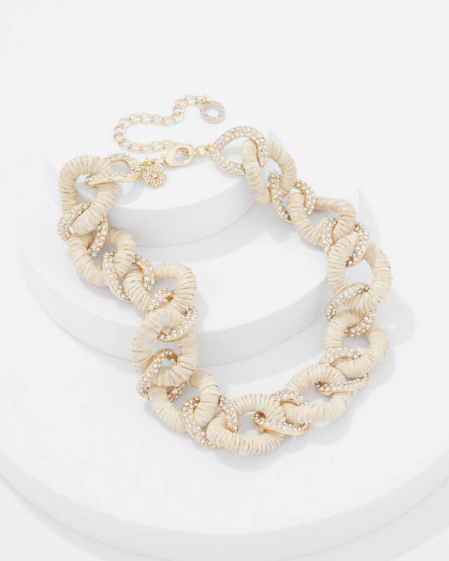 beige rope-link statement necklace with crystal-encrusted rings on a white display stand