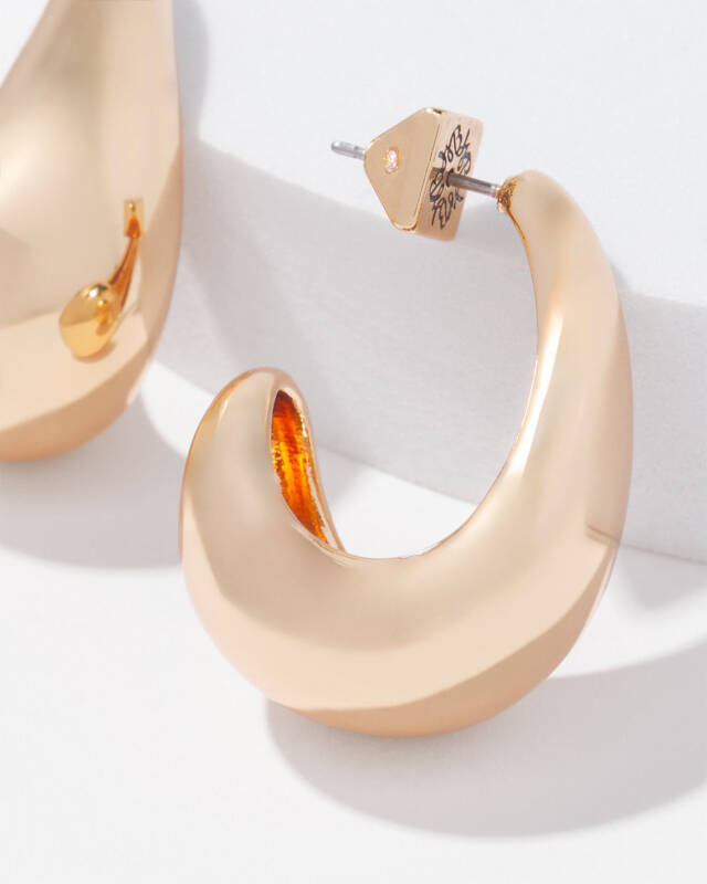 close-up of a large crescent-shaped rose-gold hoop earring on a white surface, with a stud earring in the background.