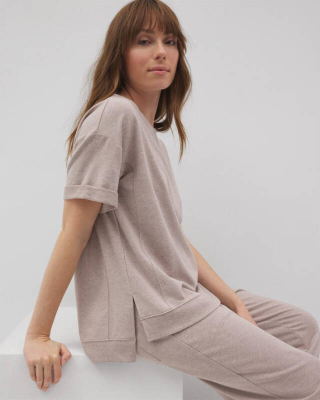 woman in a beige loungewear set (loose short-sleeve top and matching pants) sitting on a white block.