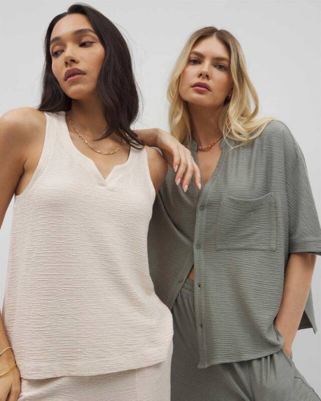 two women in textured neutral loungewear pose together; cream sleeveless top and gray button-front shirt with matching pants.