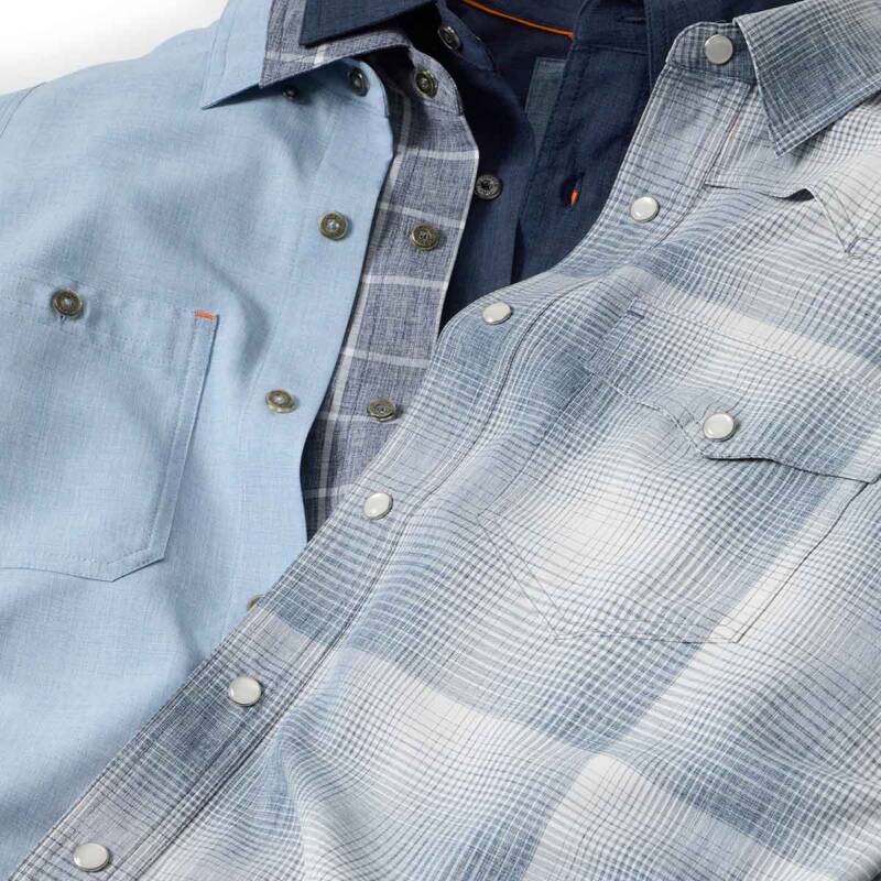 close-up of light blue and plaid button-down shirts layered together, showing collars, pockets, and metal buttons.