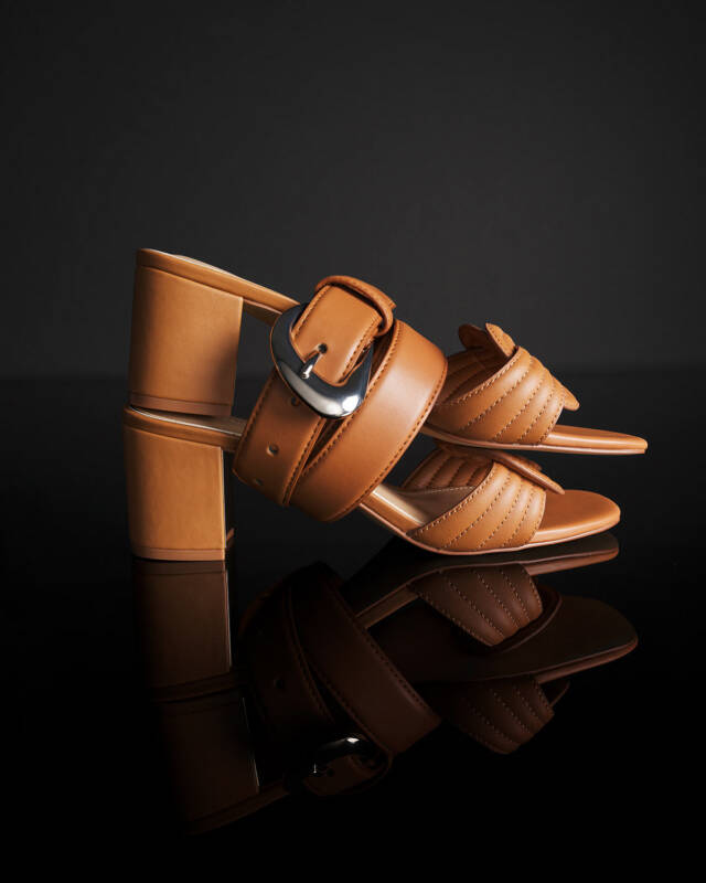 tan leather heeled sandals with a wide strap and buckle on a black glossy surface.