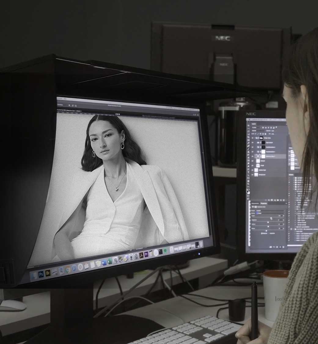 photographer or designer retouching a grayscale fashion portrait on a large monitor while using photoshop-like software at a workstation